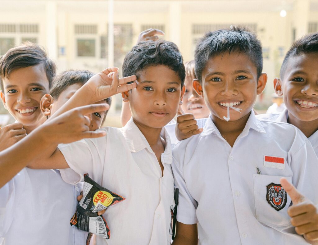 Joyful Indonesian schoolboys in white uniforms smiling and posing outdoors.