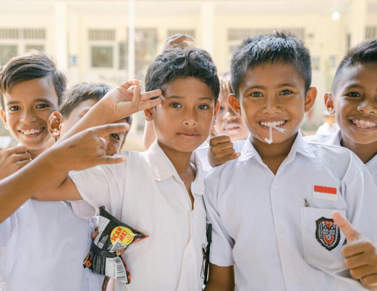 Joyful Indonesian schoolboys in white uniforms smiling and posing outdoors.