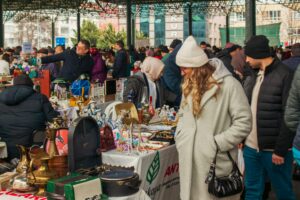 Busy outdoor bazaar with diverse vendors and shoppers exploring antique and modern items.