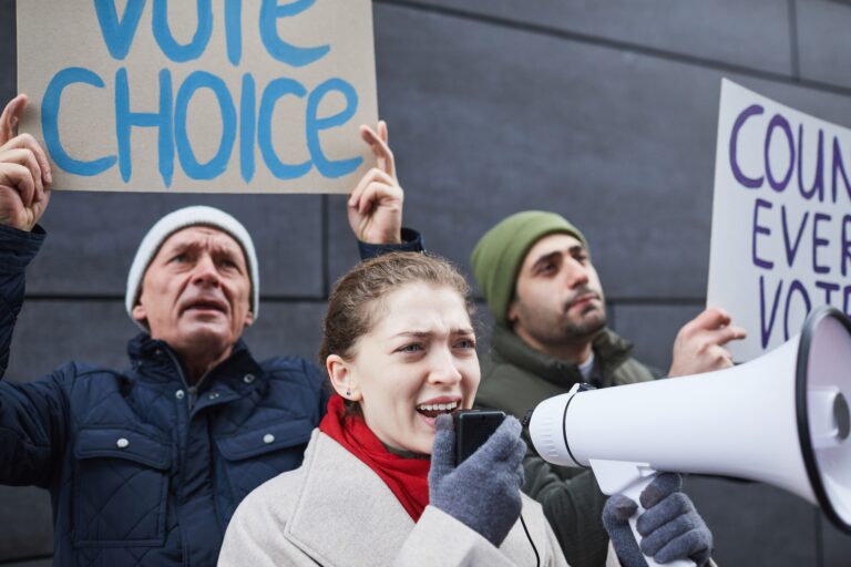 Protestors speaking out with signs and megaphone advocating for voting rights.