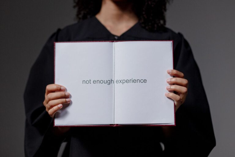 A graduate in cap and gown displays a diploma reading 'not enough experience', highlighting job market challenges.
